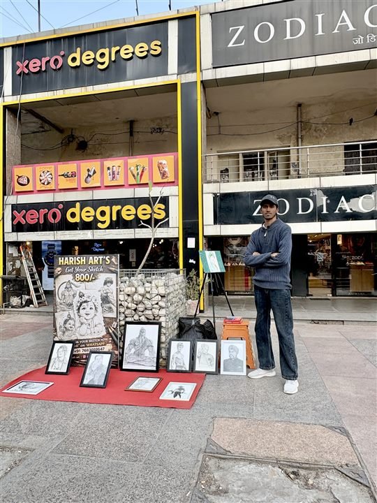 Harish Rawat standing beside his artwork stall in Noida Sector 18